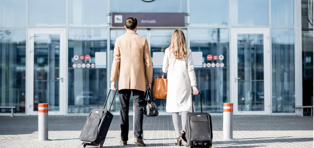 un homme et une femme sont devant un aéroport avec des valises.