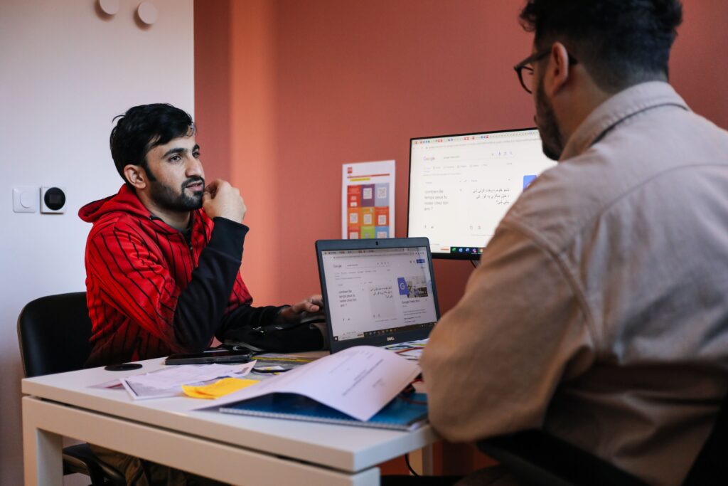 Un jeune est assis en face d'un conseiller au bureau, recevant des conseils personnalisés et un soutien attentif pour l'aider à avancer dans son parcours